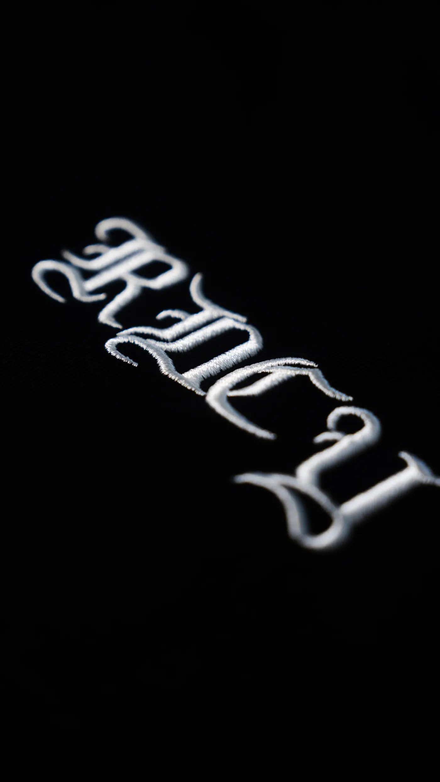 The same mark stitched on black, raked light across the satin stitch